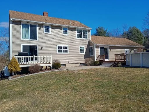 Completed rear yard view of a beige two-story home with white trim, decks, and pool