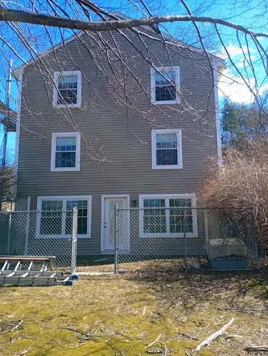 Rear of a two-story home with completed beige vinyl siding and white window trim