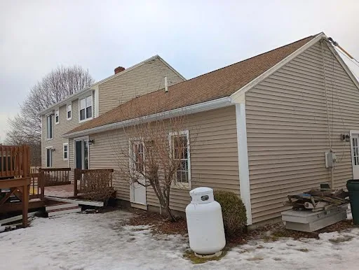 Winter side view of a beige two-story home with its deck and attached garage wing