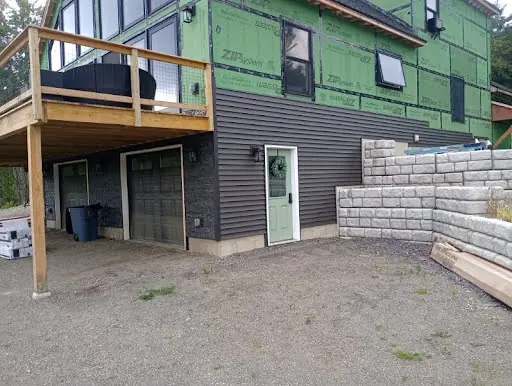 Dark siding installation in progress on a walkout-level exterior