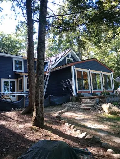Dark exterior siding renovation underway on a wooded Maine home